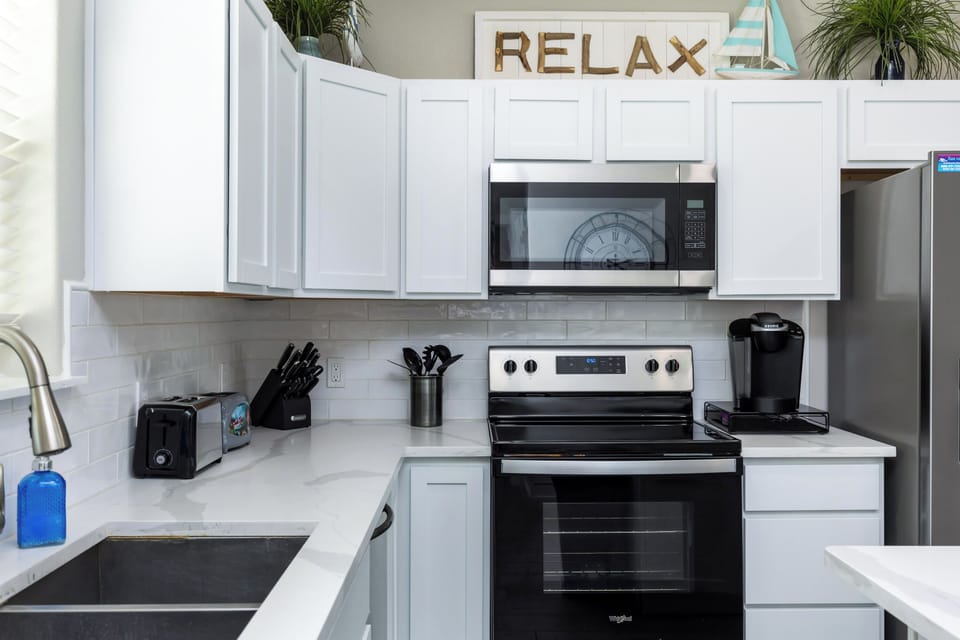 Your bright, modern kitchen invites you to cook and unwind with sleek white cabinets, stainless appliances, and peaceful 'RELAX' reminder overhead.