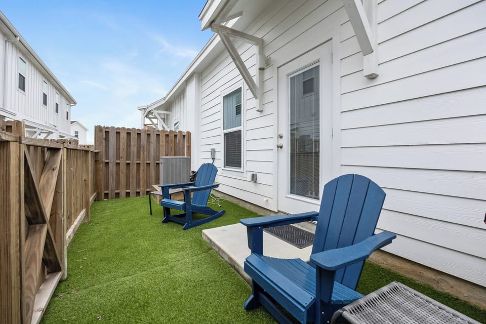 Relax in your private backyard oasis with bright blue Adirondack chairs perfect for morning coffee or evening conversations on lush green turf.