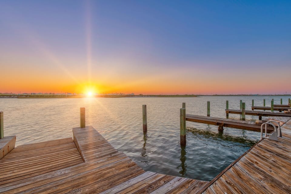 Stunning waterfront sunset paints the sky in golden hues over peaceful waters and wooden marina docks.