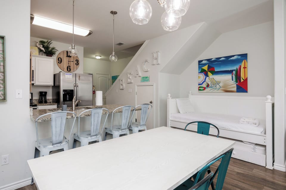 Your open-concept dining and kitchen space features coastal charm with globe pendant lights and cheerful artwork welcoming you home.