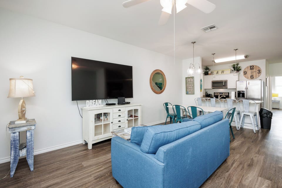 Relax in your bright living space with comfy blue seating, large TV, and open kitchen - perfect for memorable vacation moments.