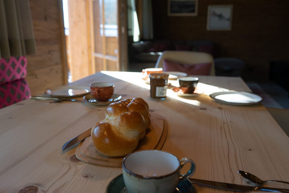 A laid breakfast table with a plaited loaf, cups and jam