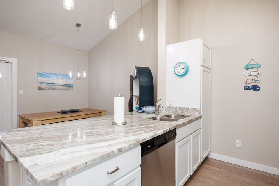 Your modern kitchen features gleaming marble countertops and sleek white cabinetry, perfect for preparing meals during your beach getaway.