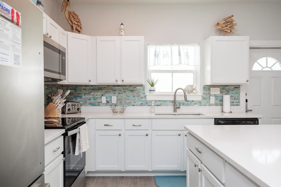 Step into your bright, fully-equipped kitchen with sparkling white countertops, coastal-inspired tile backsplash, and everything you need to create delicious meals during your stay.