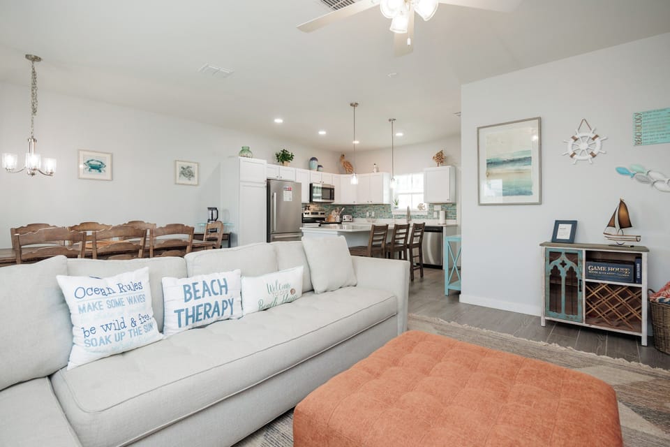 Settle into your coastal-themed living space where beach therapy pillows invite relaxation and an open kitchen awaits your culinary adventures.