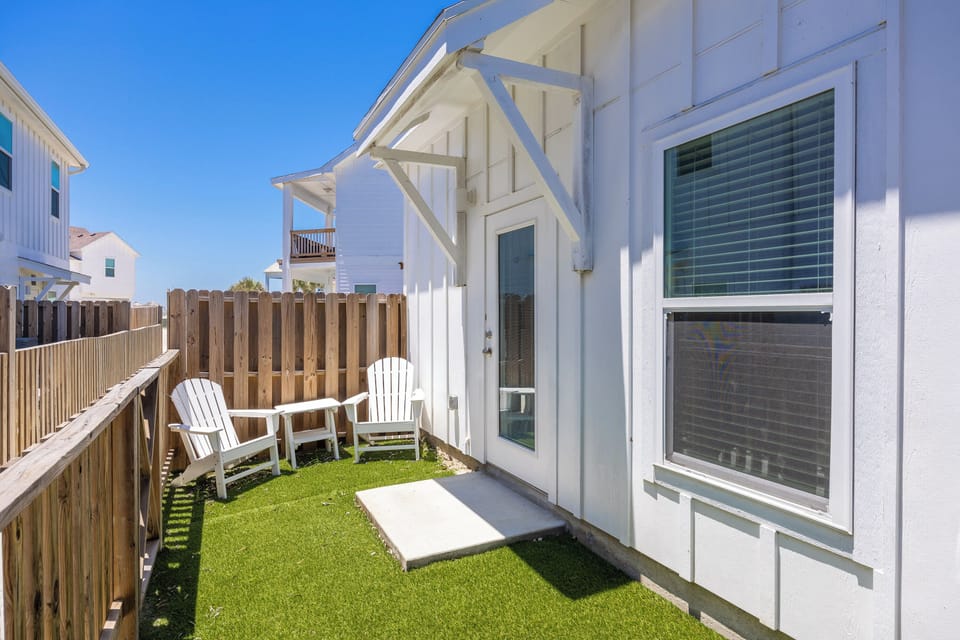 Relax in your private backyard oasis with comfortable Adirondack chairs and lush artificial turf for barefoot lounging.