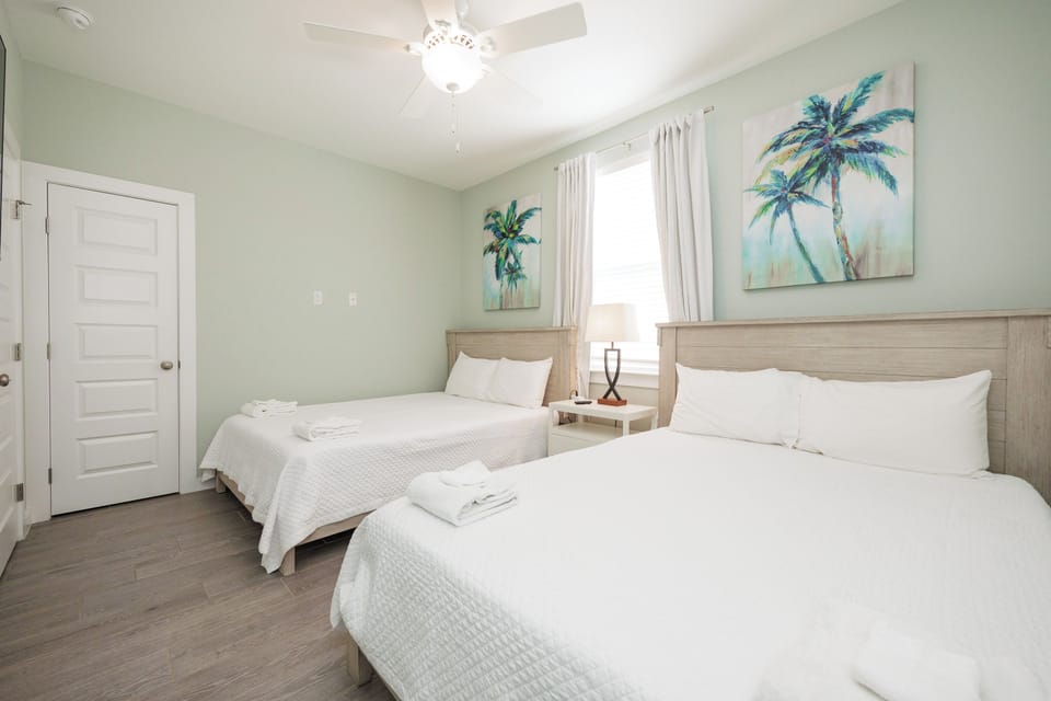 Your tropical-themed bedroom offers two comfortable beds with crisp linens, gentle ceiling fan, and beachy palm art for peaceful nights.