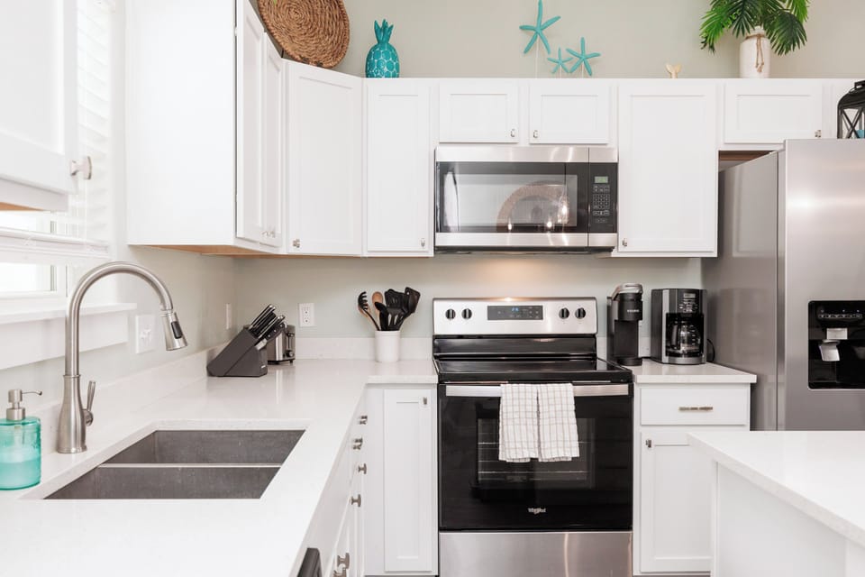 Your fully-equipped kitchen awaits with sleek white cabinets, stainless steel appliances, and coastal touches that make cooking feel like a vacation.