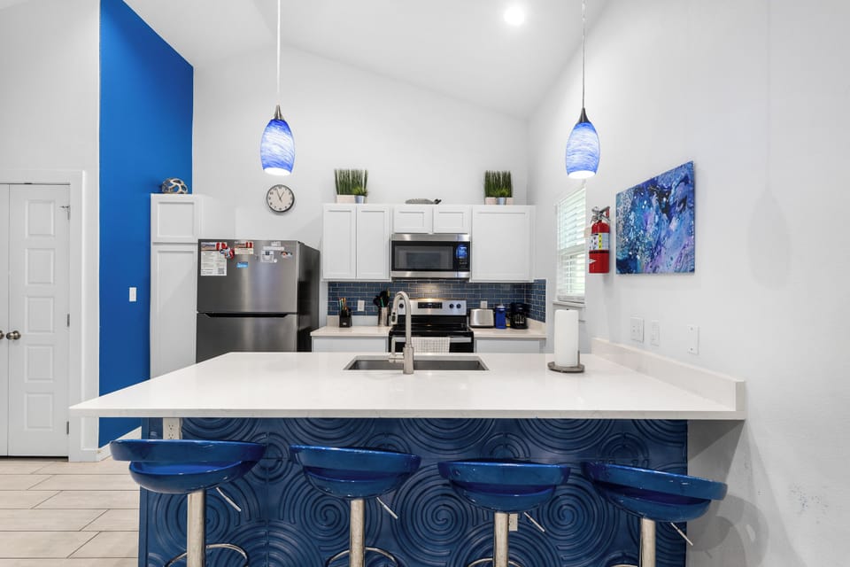 Your bright, modern kitchen features sleek stainless appliances and a stylish breakfast bar with bold blue accents—perfect for whipping up morning coffee or enjoying casual meals together.