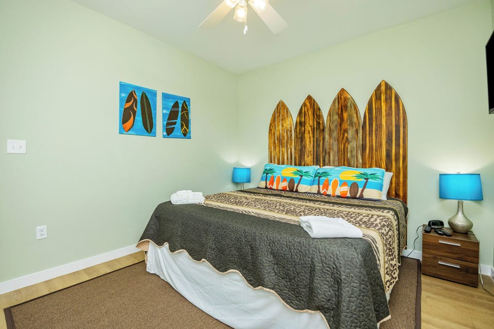 Drift off to sleep in your surf-inspired bedroom, featuring a unique wooden surfboard headboard and tropical artwork that brings beach vibes indoors.