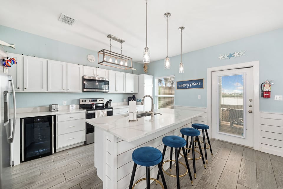 Step into your bright, coastal-inspired kitchen where soft blue tones and crisp white cabinetry set a serene mood. Gather around the spacious island with plush navy stools, perfect for morning coffee or planning your day's adventures.