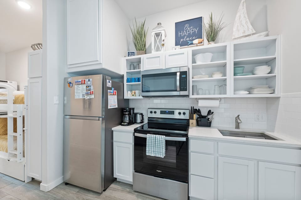 Your bright coastal kitchen features stainless steel appliances and open shelving, perfect for preparing meals with nautical charm.