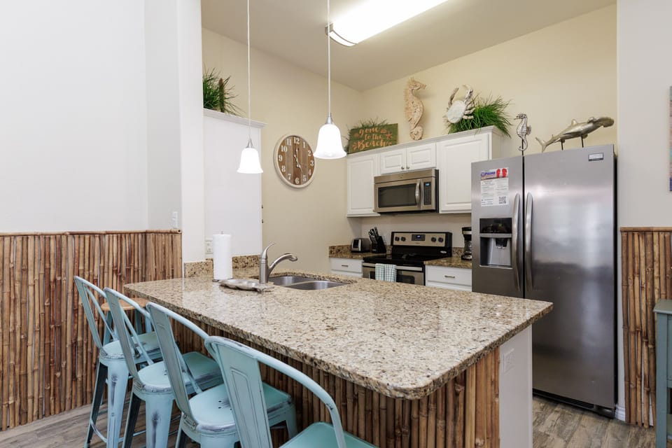 Your fully equipped kitchen features granite counters, stainless appliances, and coastal charm with bamboo accents and turquoise seating.