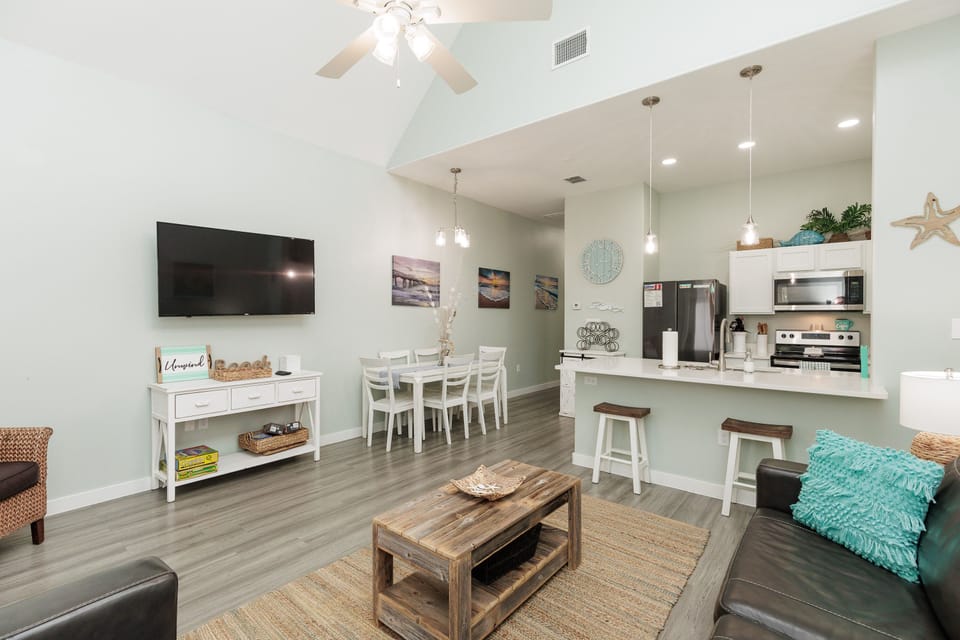 Relax in your spacious open-plan living area with coastal-themed decor, modern kitchen, and comfortable seating perfect for vacation gatherings.