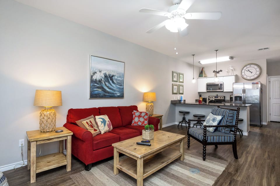 Relax in your bright open-plan space with coastal touches, featuring a plush red sofa and fully equipped kitchen for memorable stays.