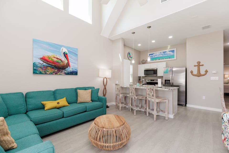 Relax in your bright open-plan living space where coastal charm meets modern comfort, featuring turquoise seating and ocean-inspired artwork.