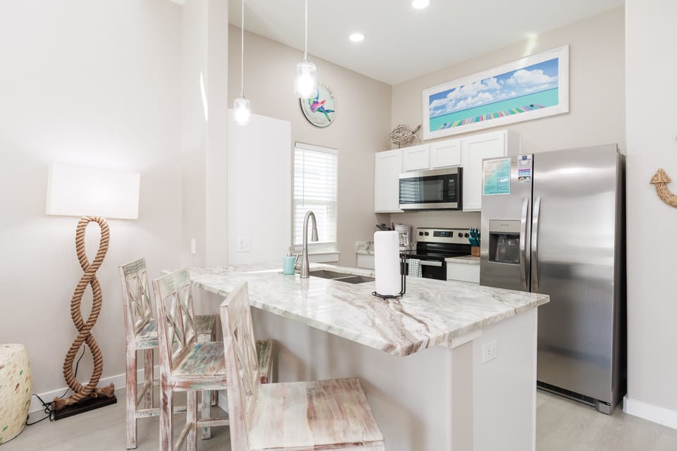 Your coastal-themed kitchen awaits with marble countertops, stainless steel appliances, and beach-inspired decor creating the perfect vacation cooking space.