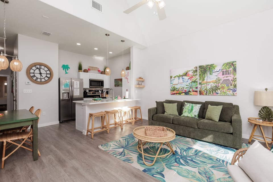 Relax in your tropical-themed living space with cozy seating, modern kitchen, and vibrant coastal artwork creating the perfect vacation atmosphere.