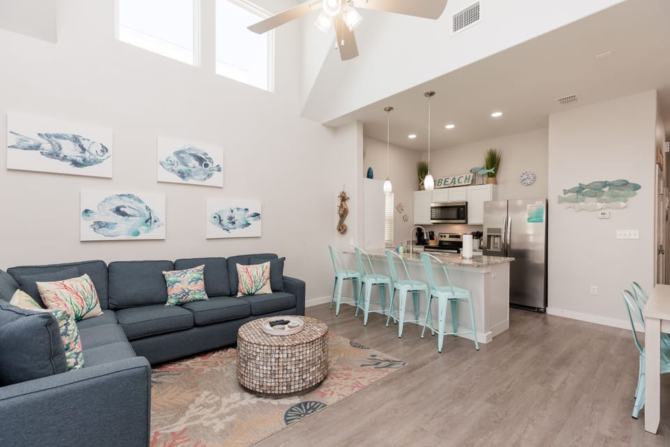 Relax in your bright, beach-themed living space with soaring ceilings, coastal artwork, and a fully equipped kitchen perfect for vacation meals.