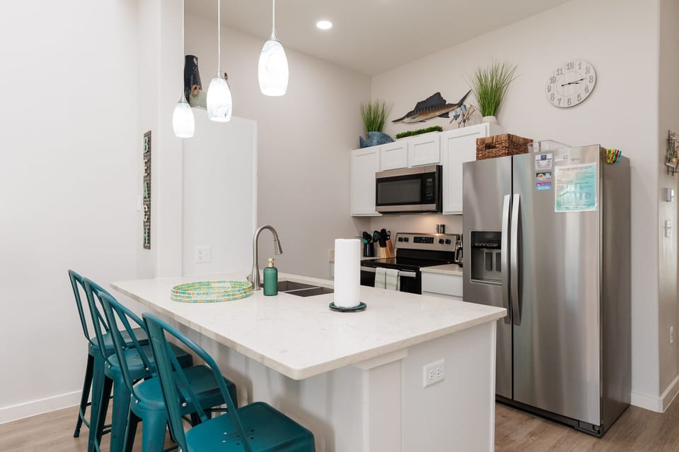 Your bright, modern kitchen features sleek white countertops, stainless steel appliances, and cheerful turquoise bar stools for casual dining.
