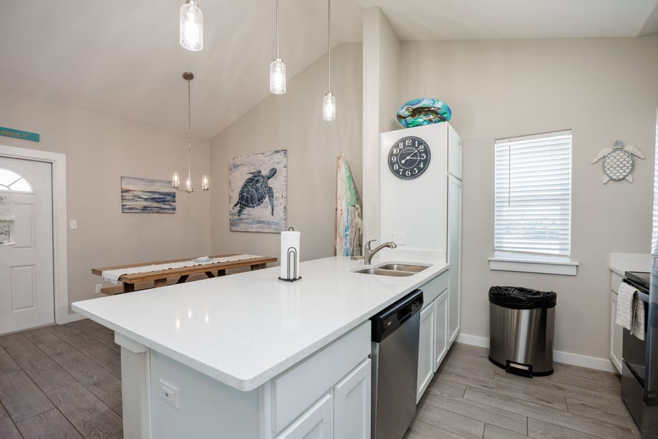Your coastal-themed kitchen invites culinary adventures with modern appliances, quartz counters, and charming sea turtle artwork creating a serene cooking atmosphere.