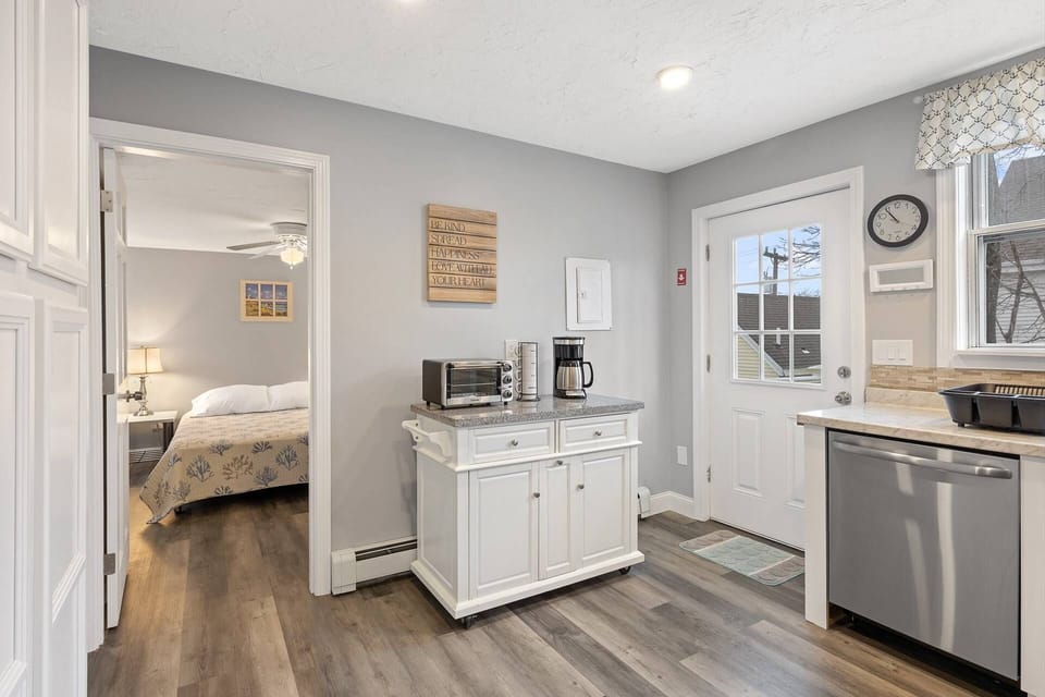 View of the kitchen with the entrance and dishwasher.  Kitchen is fully equipped with various small appliances and supplies.  There's a toaster oven,