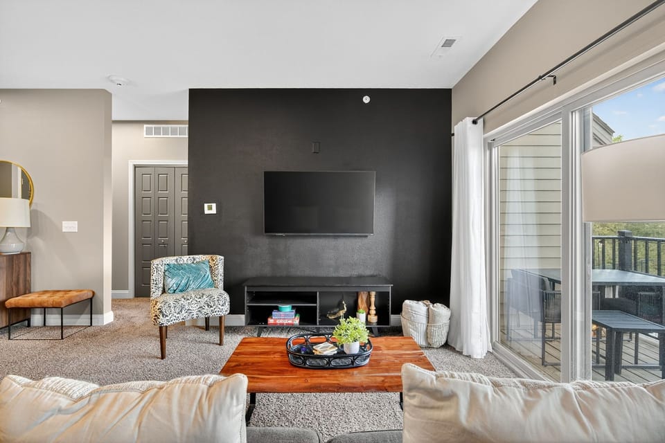 Gather in the stylish living area with bold black accent wall, mounted TV, and curated décor. Sliding doors open to a private balcony, extending your living space into the fresh air.