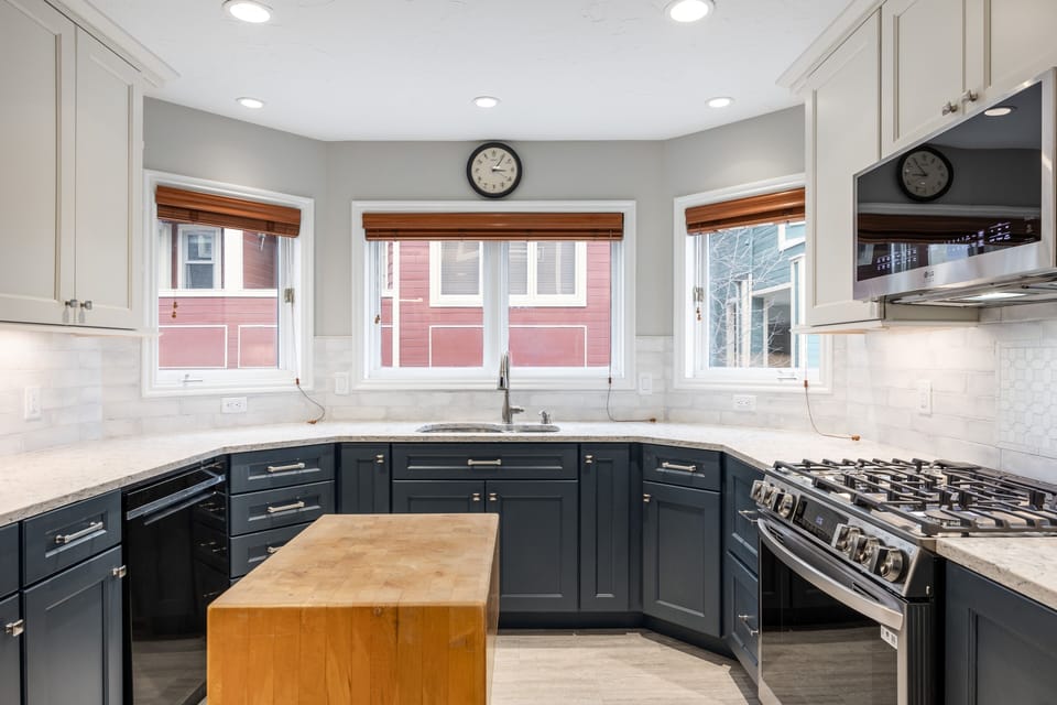- Prepare meals in a chef's dream kitchen surrounded by a trio of sunlit windows
- Enjoy a fully equipped setup with gas stove, microwave, and sleek butcher block island
- Charming navy cabinetry and quartz counters blend style with function