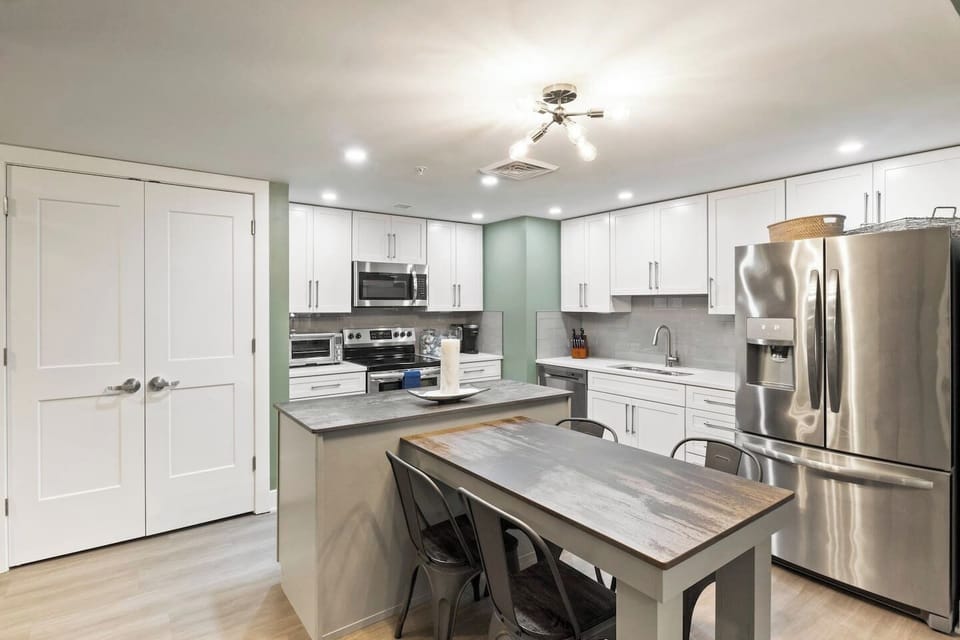 A functional kitchen with a dining area, showcasing white cabinetry and stainless steel appliances, including a refrigerator and oven. The space also features a laundry unit with a washer and dryer, cooking utensils, and a central air conditioning sy