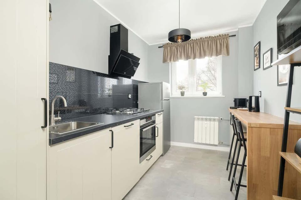 Another angle of the kitchen showcasing grey cabinetry, black backsplash tiles, and a minimalist design, maintaining a sleek and modern look.

