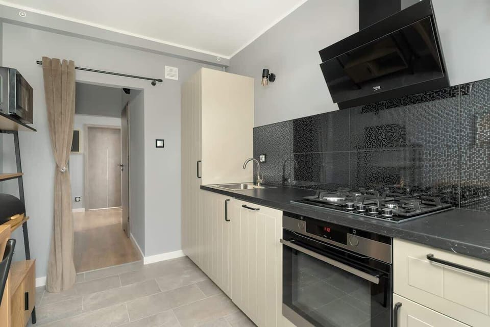 A modern kitchen with grey cabinets, black countertops, and a sleek black range hood, maintaining a contemporary and functional cooking space.
