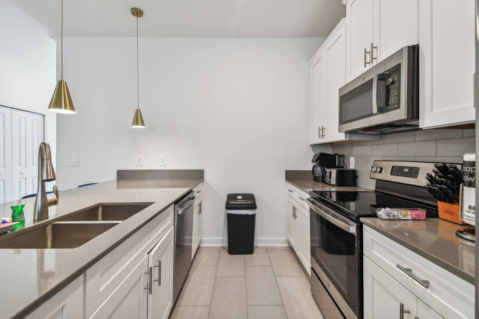 Experience the culinary charm of this stylish kitchen, complete with sleek stainless steel appliances and elegant white cabinetry. The warm glow from modern pendant lights creates an inviting space for meal prep or casual dining.