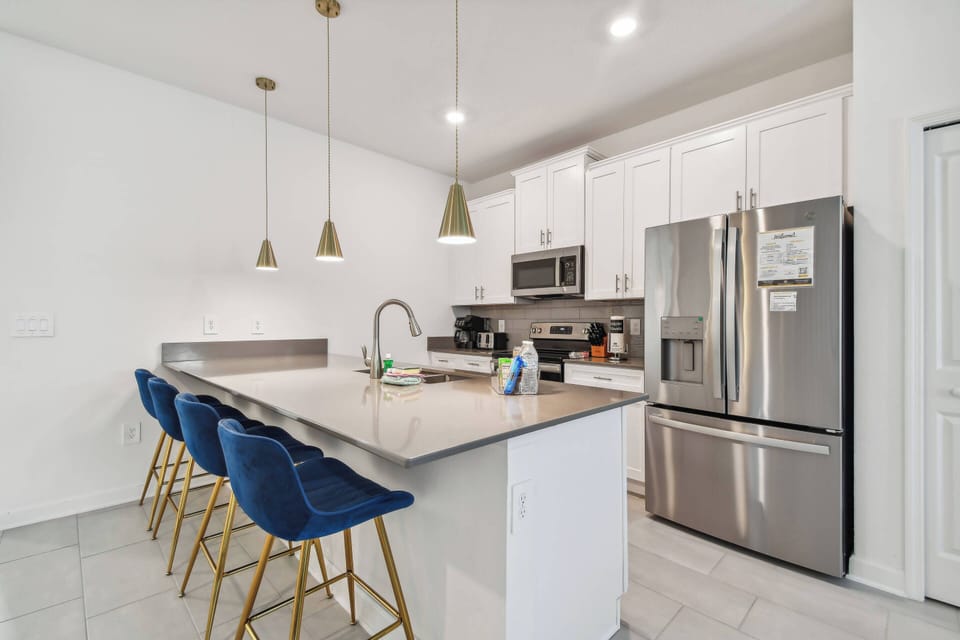 Experience a chic kitchen that combines comfort and style, featuring modern stainless steel appliances, elegant pendant lighting above a spacious island, and rich blue bar stools perfect for casual gatherings and culinary.