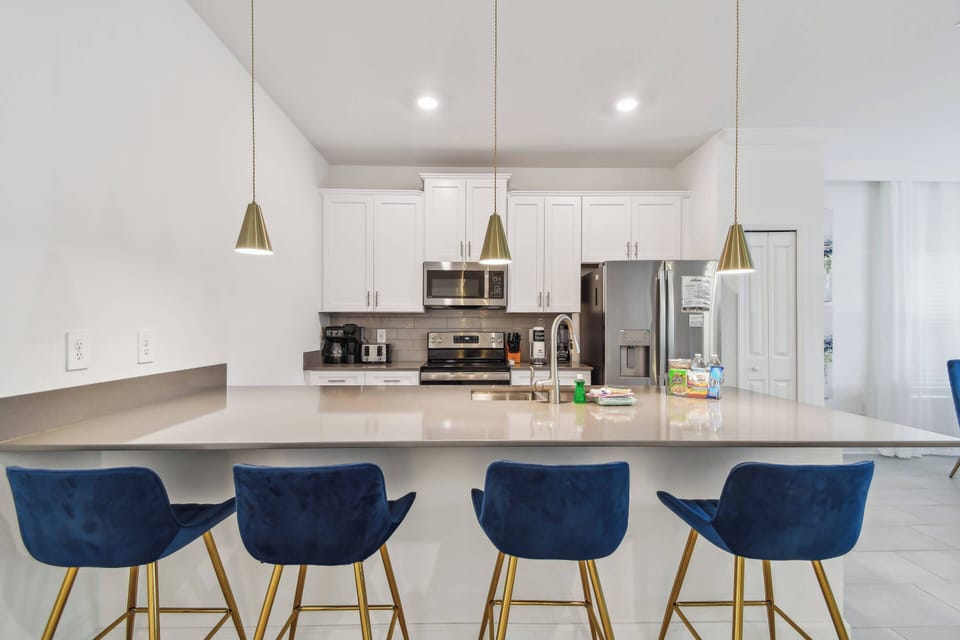 This bright kitchen features sleek white cabinetry and a spacious island with chic navy bar stools, perfect for casual meals or chats, while modern stainless steel appliances inspire your culinary creativity in style.