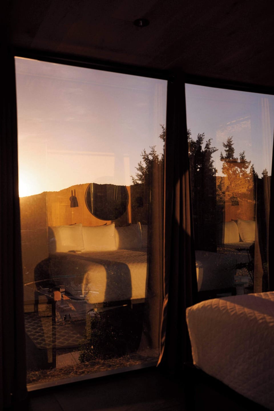 Warm evening light inside the Mirror House, with a cozy bed, dining area, and floor-to-ceiling windows surrounded by canyon scenery.