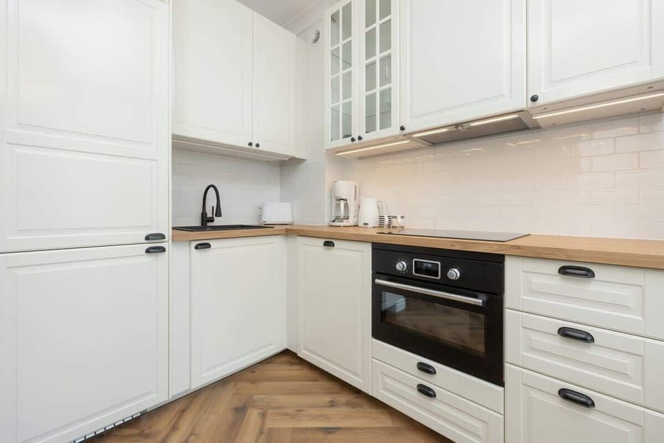 A sleek kitchen with white cabinets, wooden countertops, and modern appliances.

