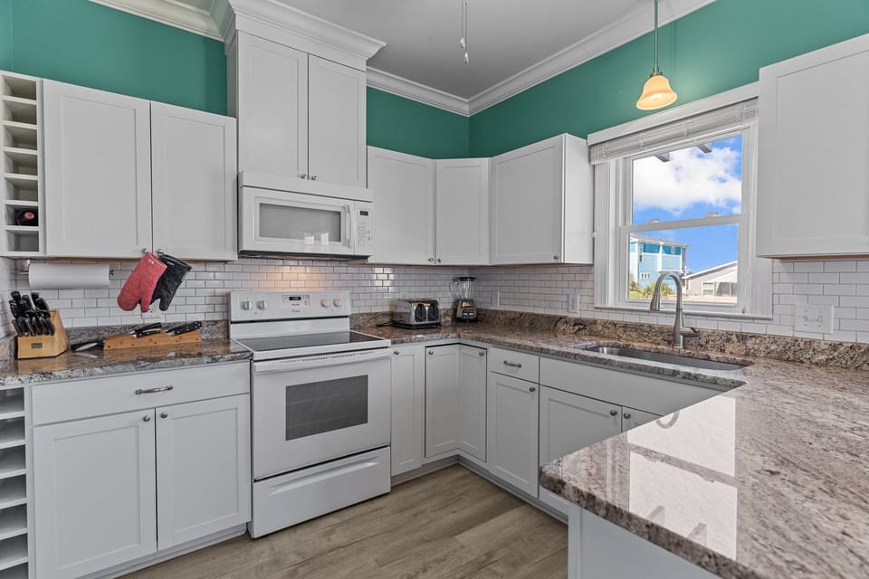 Oak Island, NC kitchen with teal walls, white cabinets, granite island, stove, microwave, sink, stools, coffee décor, subway tile, and beachy style.