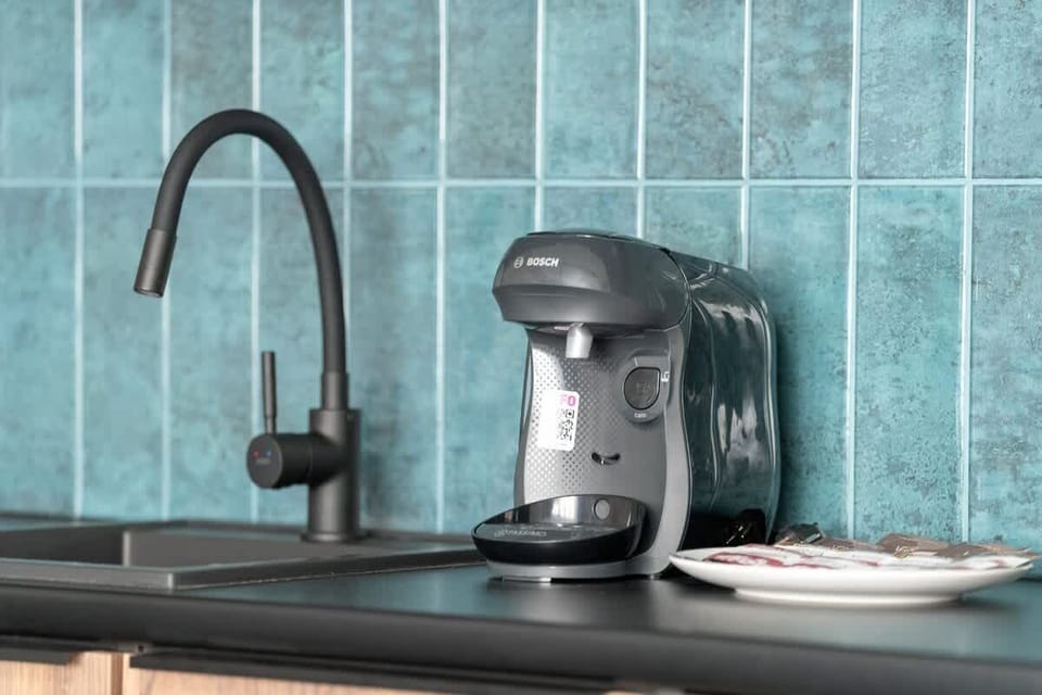 A close-up of the kitchen counter with a black coffee machine and a teal tiled backsplash.

