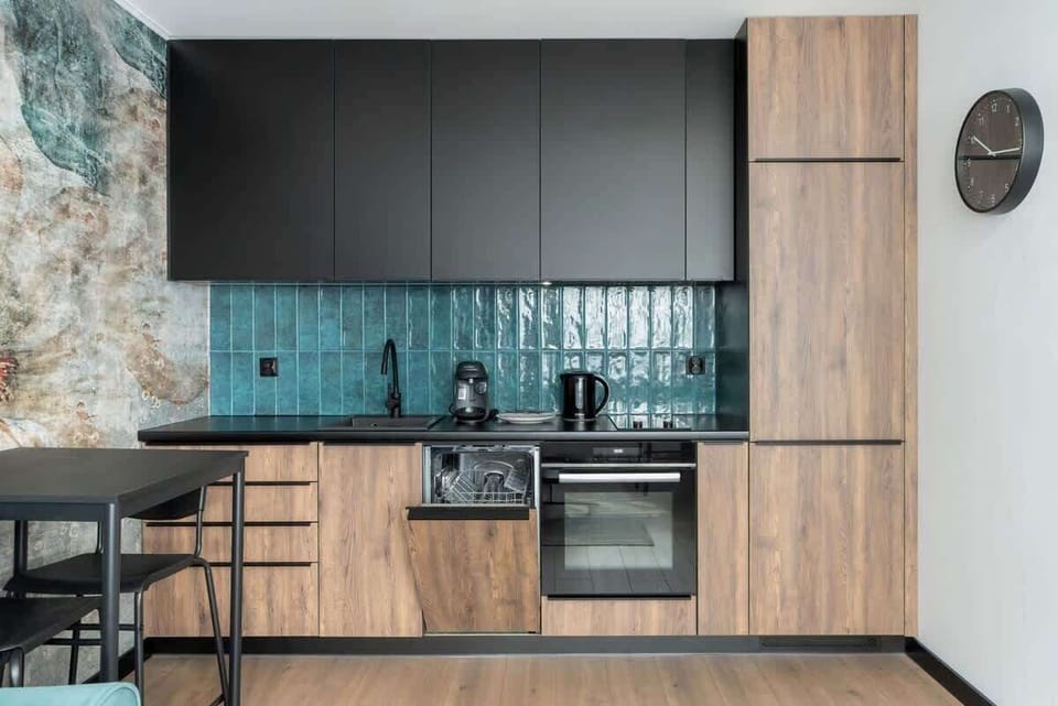A functional kitchen space with a modern black and wooden design, featuring a teal backsplash.

