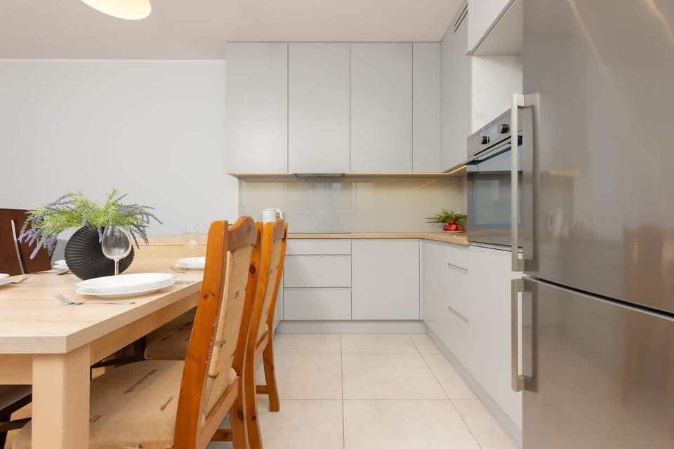 A modern kitchen with white cabinets, wooden dining table, and built-in appliances, creating a sleek and practical cooking space.

