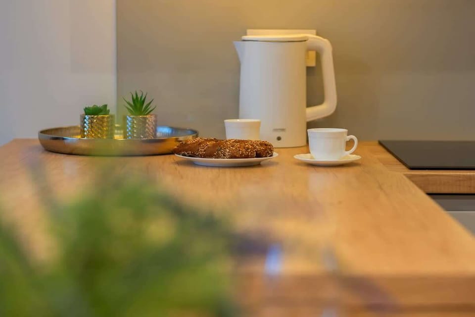 A close-up of a wooden table with a coffee setup, including a French press, cups, and greenery, creating a cozy morning atmosphere.
