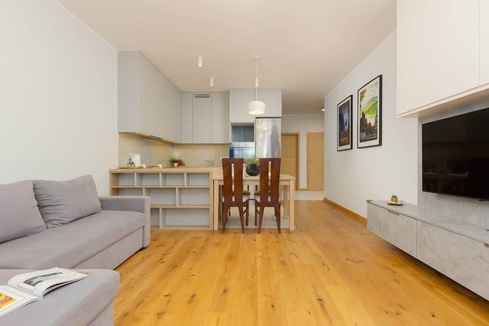 An open living and dining area with a grey sofa, wooden flooring, and a dining table, creating a warm and functional social space.

