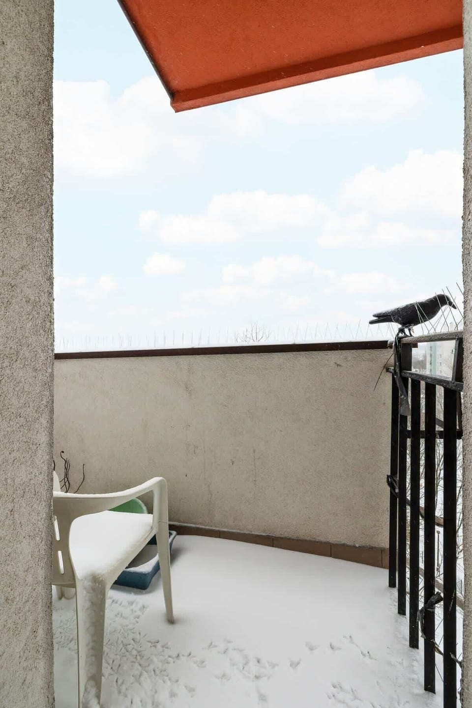 A snow-covered balcony with minimalist railing and a small outdoor chair, offering a cozy and private outdoor space.
