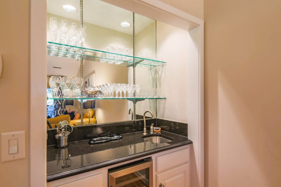 This wet bar with a drink refrigerator, sink and glassware is located within the living room.