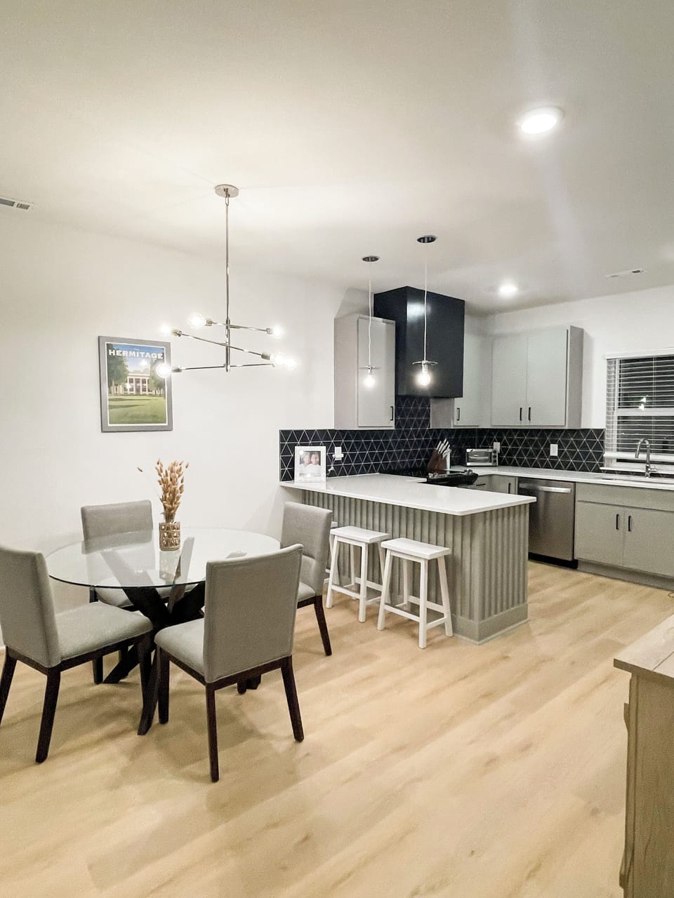 KITCHEN - This kitchen and dining area features a modern design with a sleek, stylish lighting fixture above the table, providing an inviting space for meals and gatherings. The island offers additional seating and counter space, perfect for casual dining or food preparation. The open layout is ideal for hosting and enjoying time together.