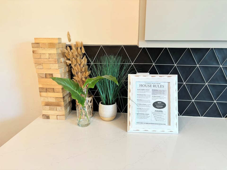 HOUSE RULES – The home’s house rules are neatly framed and displayed in the kitchen, offering guests a clear and welcoming guide for their stay. From Wi-Fi details to property guidelines, everything is easy to access, ensuring a smooth and enjoyable experience for all visitors. The decor surrounding the frame adds a natural and stylish touch, blending perfectly with the modern kitchen setting.