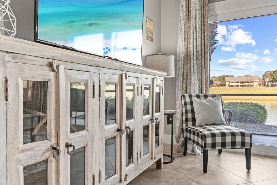 Coastal-inspired living space with stylish décor, a large flatscreen TV, comfortable seating, and peaceful lake views.