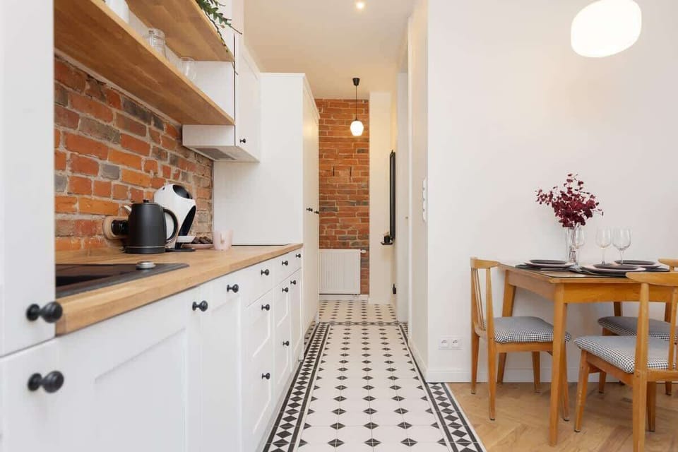 A modern kitchen with white cabinets, wooden countertops, and a brick accent wall, creating a blend of contemporary and rustic design.
