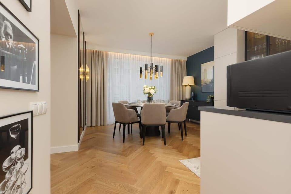 Open dining and living area with framed artwork, wooden parquet flooring, and elegant pendant lighting.
