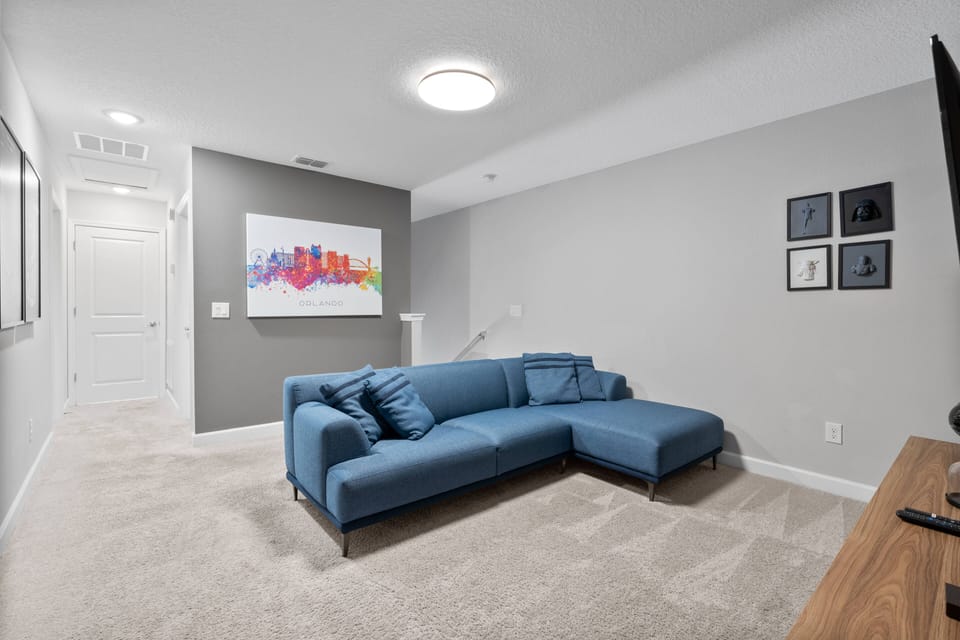 Unwind in the spacious living area, complete with a sleek blue sectional sofa and soft, neutral walls. The cozy atmosphere is enhanced by plush carpet and vibrant artwork, making your stay truly memorable and inviting.